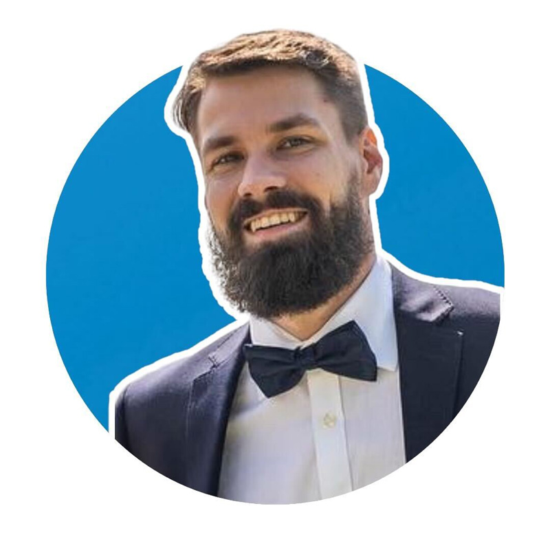 Man with a beard and a bow tie smiling, wearing a suit jacket and white shirt, with a blue circular background.